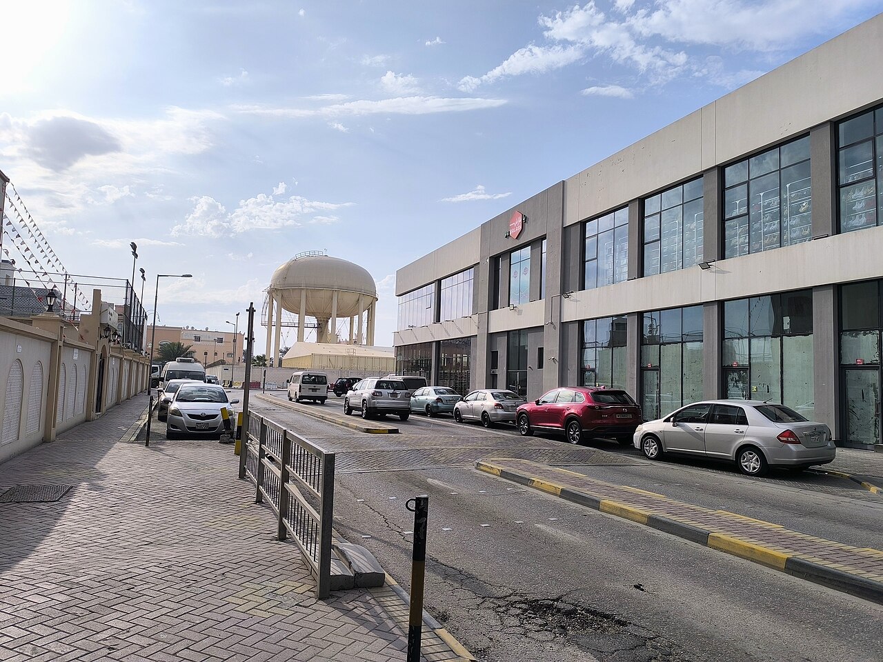 شارع في المحرق بمبانٍ وسيارات وخزان مياه مرتفع في الخلفية